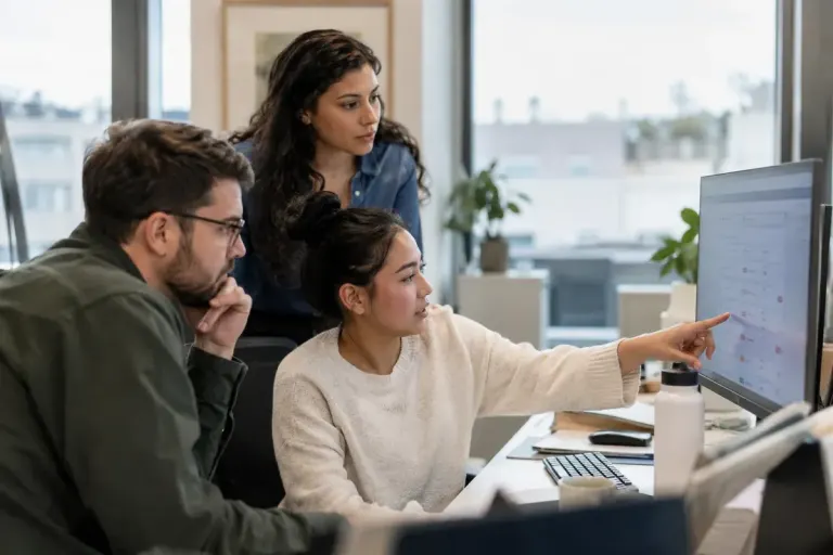 Operations team reviewing a short flagged-work queue on a shared monitor in an office, screen text indistinct.